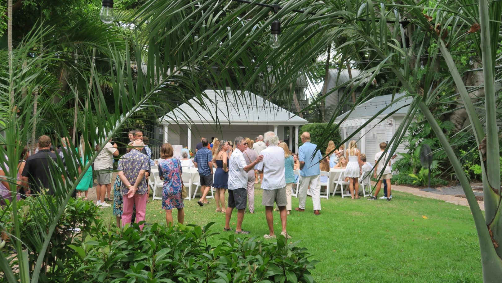 A gathering of people in a lush garden near a gazebo surrounded by greenery.