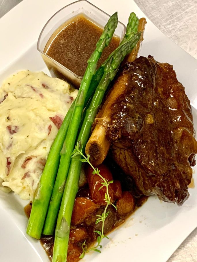 A plate featuring braised meat, mashed potatoes, asparagus, and a sauce.