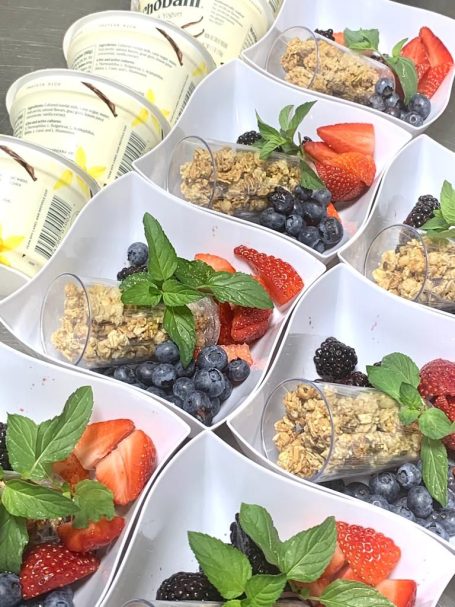 Breakfast Parfait Four dessert cups with granola, berries, and mint, alongside two tubs of cream.
