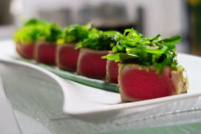 Sesame Tuna Sliced seared tuna with green garnish arranged on a white plate.
