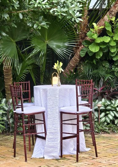 Outdoor setting with a small round table, three high chairs, and lush greenery.