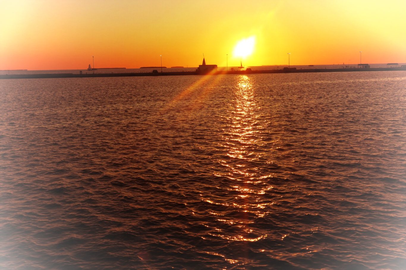 Key West Sunset Dockside Event Sunset over calm waters, with a city silhouette in the background and warm orange hues.