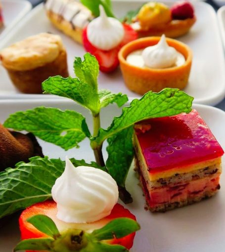 An assortment of colorful desserts including layered cakes, tarts, and fresh fruit.