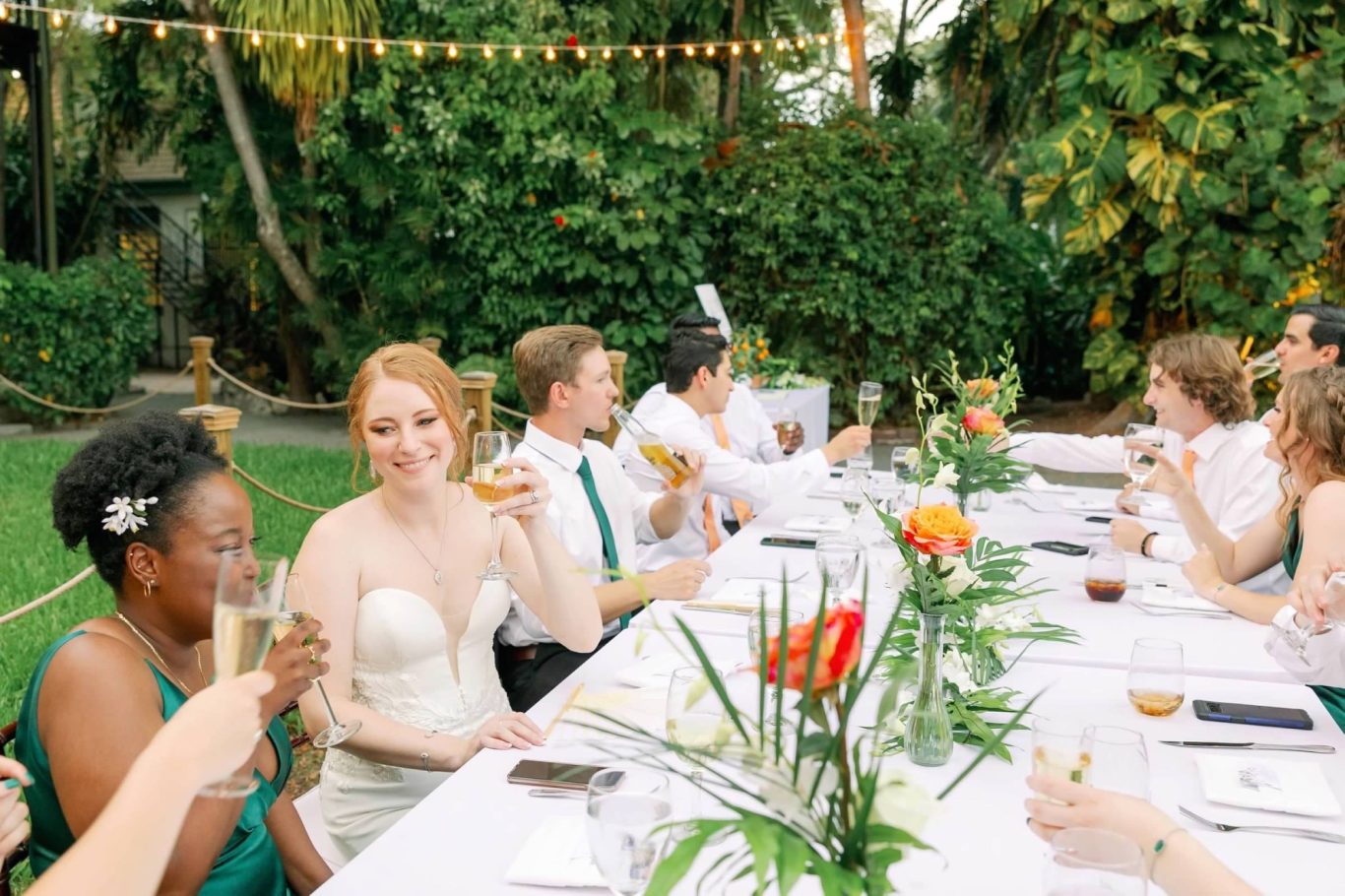 A wedding reception with guests toasting at a long table decorated with flowers.